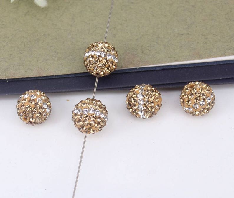 May include: Five gold-toned round beads with clear rhinestones. The beads are strung on a silver wire.