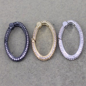 May include: Three oval-shaped metal clasps with a clear crystal embellishment. The clasps are in black, gold, and silver.