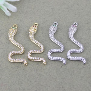 May include: Four snake-shaped charms with clear crystal accents. Two charms are gold-toned and two are silver-toned. Each charm has a small green or red stone on the head.
