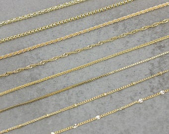 May include: A collection of ten gold chains of different styles and thicknesses, laid out in a row on a gray surface.