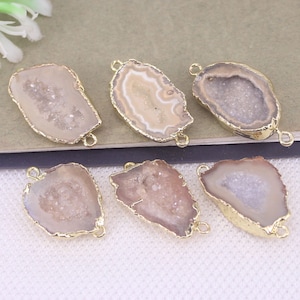 May include: Six natural stone pendants with gold-colored edges. The pendants have a geode-like appearance, with a mix of beige, brown, and white colors. Each pendant has a small loop at the top and bottom for attaching to jewelry.