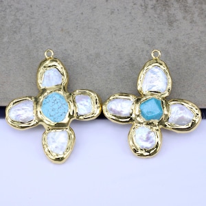 Puede incluir: Dos colgantes dorados en forma de cruz. Cada colgante presenta una piedra turquesa central rodeada de cuatro perlas blancas de forma irregular. Los bordes de las cruces tienen un acabado dorado texturizado, y cada una tiene un pequeño lazo en la parte superior para colgar.