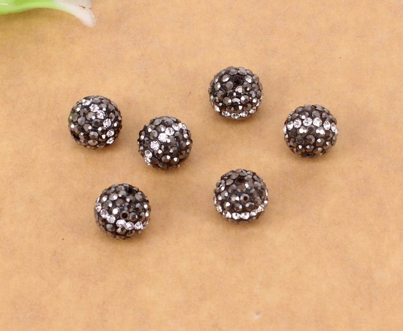 May include: Seven black round beads with a silver sparkle finish. Each bead is covered in small, closely spaced rhinestones.