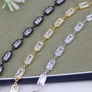 May include: Three strands of chain with rectangular clear crystal accents. The chains are black, gold, and silver.