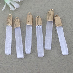 Puede incluir: Seis colgantes de cristal de selenita blanca con tapas chapadas en oro. Los cristales son rectangulares y tienen un acabado liso y pulido.
