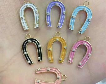 Puede incluir: Surtido de dijes de herradura de esmalte de colores con detalles dorados y diamantes de imitación transparentes. Cada dije presenta un esmalte de color diferente, incluyendo blanco, morado, azul, negro, amarillo, rosa y rosa claro.