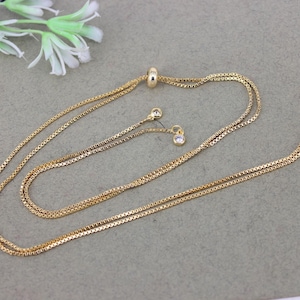 May include: A gold chain necklace with a sliding clasp and two small clear crystal accents.