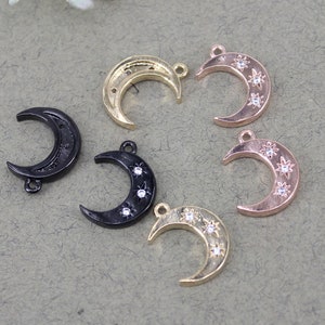 Pode incluir: Cinco pingentes de lua crescente com detalhes de estrelas. Os pingentes s&atilde;o de metal dourado, ouro rosa e preto.
