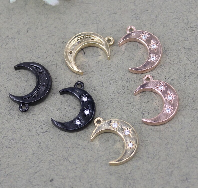 Pode incluir: Cinco pingentes de lua crescente com detalhes de estrelas. Os pingentes s&atilde;o de metal dourado, ouro rosa e preto.
