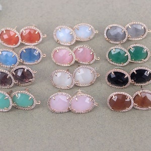 May include: Set of 12 pairs of oval-shaped earrings with a faceted design. The earrings are made of gold-tone metal and feature a variety of colors, including pink, green, blue, gray, and brown.