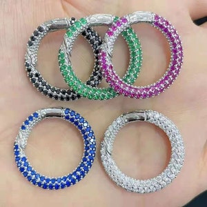 Könnte beinhalten: Fünf silberne Ringe mit verschiedenen Edelsteinen. Die Ringe sind mit kleinen runden Steinen besetzt. Die Farben der Steine sind schwarz, grün, rosa, blau und weiß.