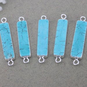 May include: Five turquoise blue rectangular pendant charms with silver-toned metal loops on each end. The charms are made of natural turquoise stone with a marbled pattern.