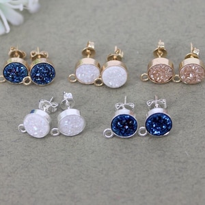 Puede incluir: Seis pares de pendientes con cabujones de piedras preciosas de diferentes colores. Los pendientes están hechos con engastes de metal dorado y plateado. Las piedras preciosas son azules, blancas y marrones.