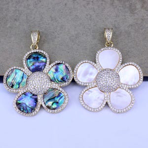 May include: Two gold flower-shaped pendants with a white and a blue and green abalone shell design. Both pendants are adorned with clear rhinestones.