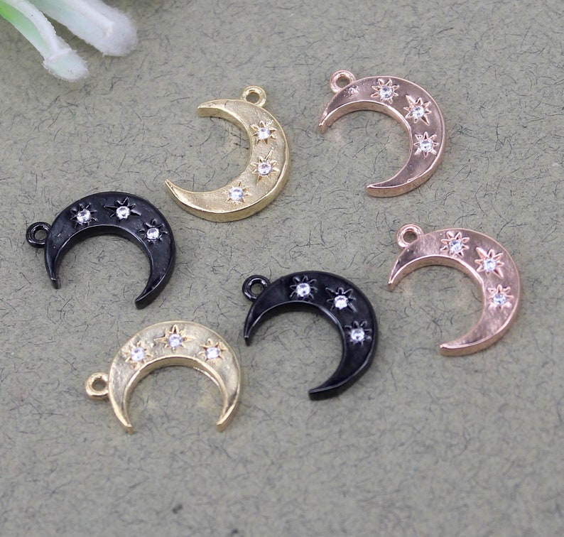 Pode incluir: Seis pingentes em forma de lua crescente com um design de estrela. Os pingentes est&atilde;o em tr&ecirc;s acabamentos diferentes: ouro, preto e ouro rosa.