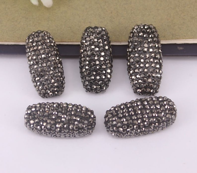 May include: Five black, rectangular, faceted beads made of rhinestones. The beads are approximately 1 inch long and 1/2 inch wide.