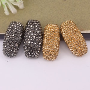 May include: Four rectangular-shaped beads, two are black with a sparkly finish, and two are gold with a sparkly finish.