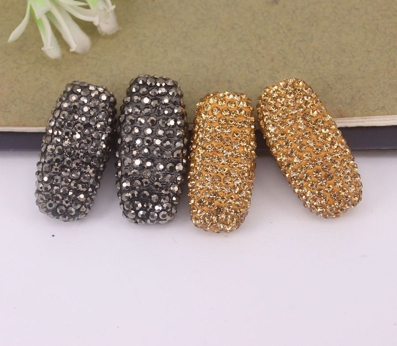 May include: Four rectangular-shaped beads, two are black with a sparkly finish, and two are gold with a sparkly finish.