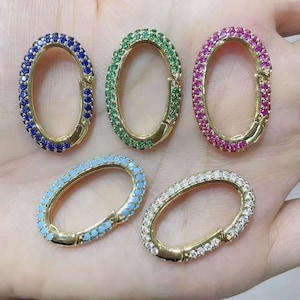 May include: Five oval-shaped clasps with different colored gemstones. The clasps are made of gold metal and have a spring-loaded closure. The gemstones are blue, green, pink, light blue, and clear.