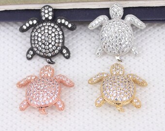 May include: Four turtle charms with a pave setting of clear rhinestones. The turtles are in black, silver, gold, and rose gold.