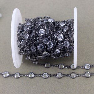 May include: A black chain with clear round beads. The chain is wound around a white spool.