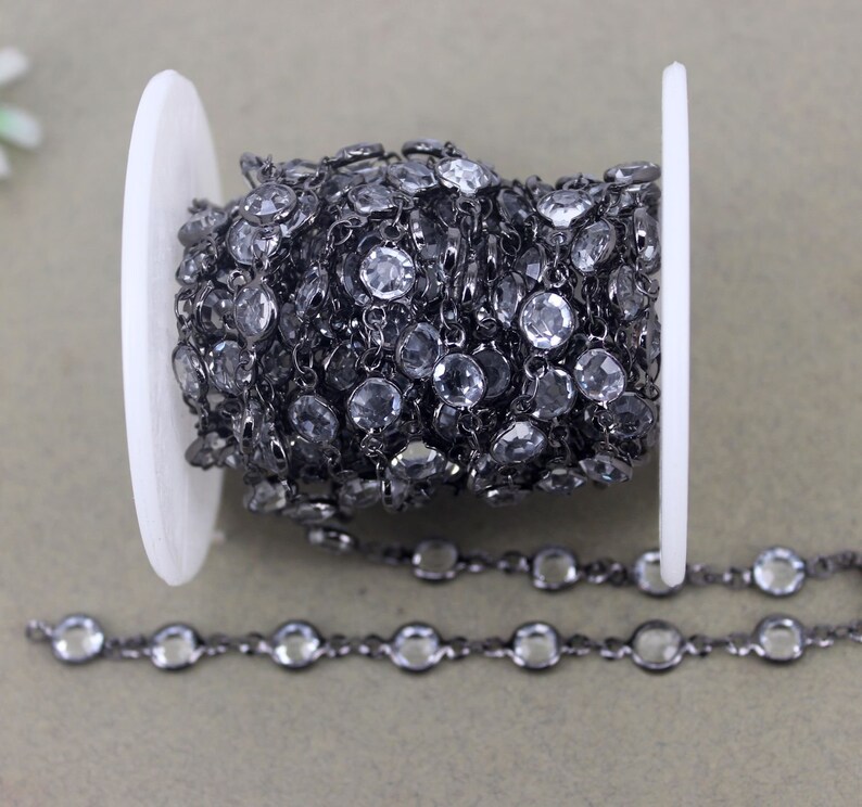 May include: A black chain with clear round beads. The chain is wound around a white spool.
