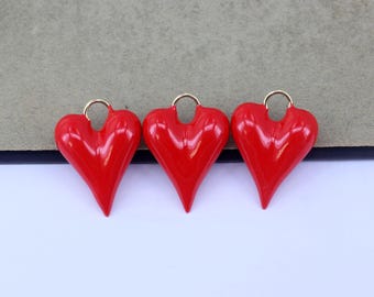 Könnte beinhalten: Drei rote herzförmige Anhänger mit goldenen Sprungringen. Die Anhänger sind glänzend und haben eine leicht erhabene Textur.