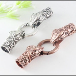 May include: Two snake head toggle clasps, one silver and one copper. The clasps are detailed with textured scales and have a ring for attaching to a cord or chain.