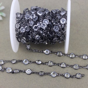 May include: A roll of black chain with clear faceted glass beads. The chain is on a white spool and there are three strands of the chain laid out on a gray surface.