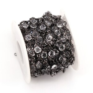 May include: A spool of black chain with clear round rhinestones. The chain is wound around a white spool.