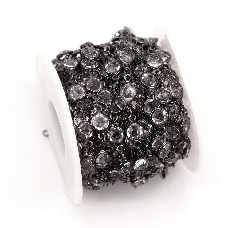 May include: A spool of black chain with clear round rhinestones. The chain is wound around a white spool.