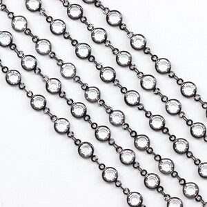 May include: A close-up of a black chain with clear round crystals. The chain is made of metal and has a shiny finish.