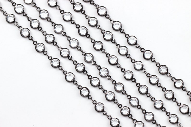 May include: A close-up of a black chain with clear round crystals. The chain is made of metal and has a shiny finish.