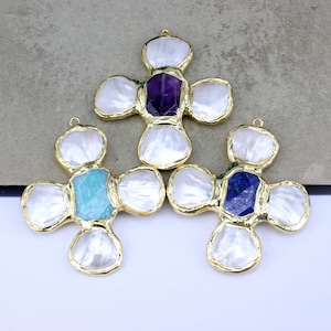 May include: Three gold-toned cross pendants with different colored gemstone centers. Each cross has a pearly white, petal-like design around the gemstone. The gemstones are purple, turquoise, and dark blue. Each pendant has a small loop at the top.