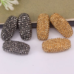 May include: A set of six oval-shaped rhinestone beads. Three beads are black and three beads are gold.