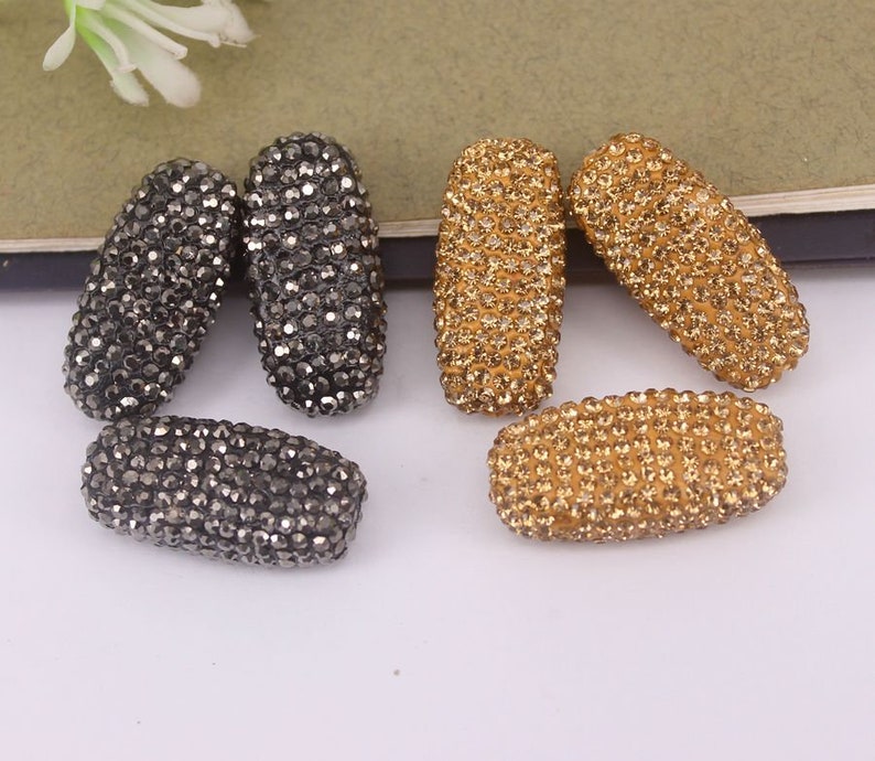 May include: A set of six oval-shaped rhinestone beads. Three beads are black and three beads are gold.