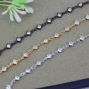 May include: Three chains with square-shaped clear rhinestones. The chains are silver, gold, and black.