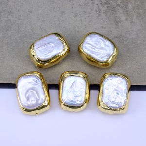 Op de afbeelding: Vijf witte barokparels met gouden metalen frames. De kralen zijn rechthoekig en hebben een licht onregelmatige vorm.
