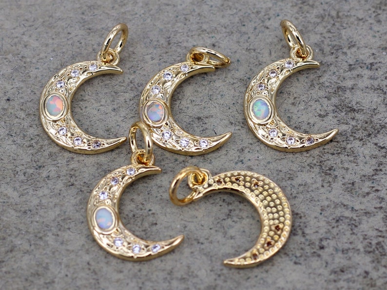 May include: Five gold crescent moon charms with opal stones and clear rhinestones. The charms have a textured surface and are perfect for jewelry making.