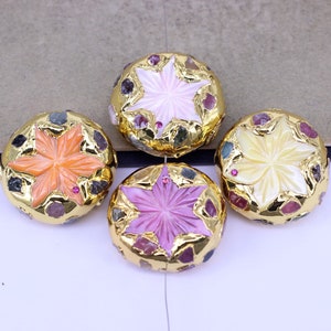 May include: Four round, gold-toned, decorative buttons with a star-shaped design in the center. Each button features a different color: pink, orange, yellow, and purple. The buttons are surrounded by small, colorful gemstones.