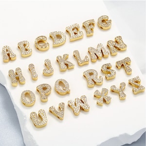 May include: A set of 26 gold-tone alphabet letter charms, each letter is encrusted with clear sparkling rhinestones. The charms are perfect for adding a personalized touch to jewelry projects.