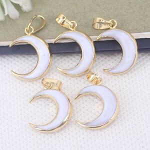 Pode incluir: Quatro pingentes de lua crescente banhados a ouro com esmalte branco. Cada pingente tem um laço para prender a uma corrente ou cordão.