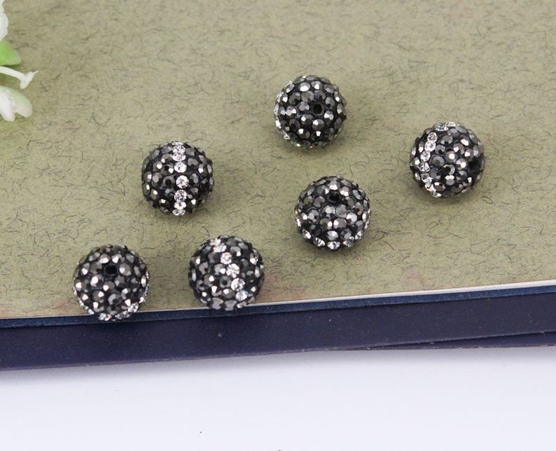 May include: Six black and silver round beads with a sparkly finish. The beads are arranged on a light brown surface.