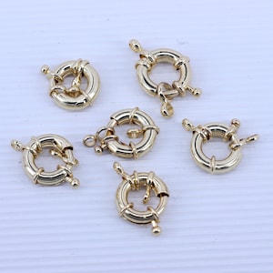 May include: Six gold-toned metal clasps for jewelry making. Each clasp is a round ring with a twisted design.
