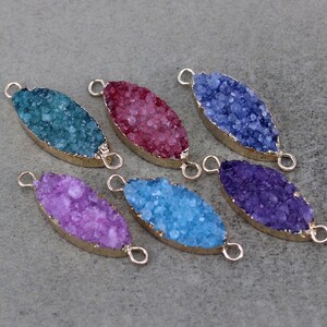 May include: Six oval-shaped crystal charms with gold-toned metal connector loops. The charms are in shades of teal, pink, blue, purple, and light blue.