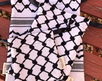 May include: White fabric bags with a black geometric pattern and black ribbon ties. The bags are in various sizes and have a label that reads "ASHKAL ALWAN". The bags are displayed on a red wooden bench.