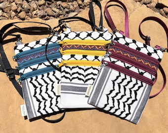 May include: Three small crossbody bags with black straps and zippers. The bags have a white background with black geometric patterns and colorful zipper accents in teal, yellow, and burgundy. The bags are made of fabric.