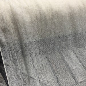 May include: A roll of white sheer fabric with a fine mesh texture. The fabric is draped over a wooden surface.