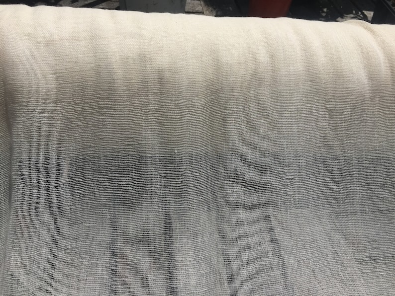 May include: A close-up of a white, sheer fabric with a subtle ombre effect. The fabric has a fine, woven texture and appears to be lightweight and airy.