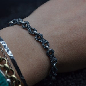 May include: A silver bracelet with a textured, chain-link design. The bracelet is worn on a person's wrist.
